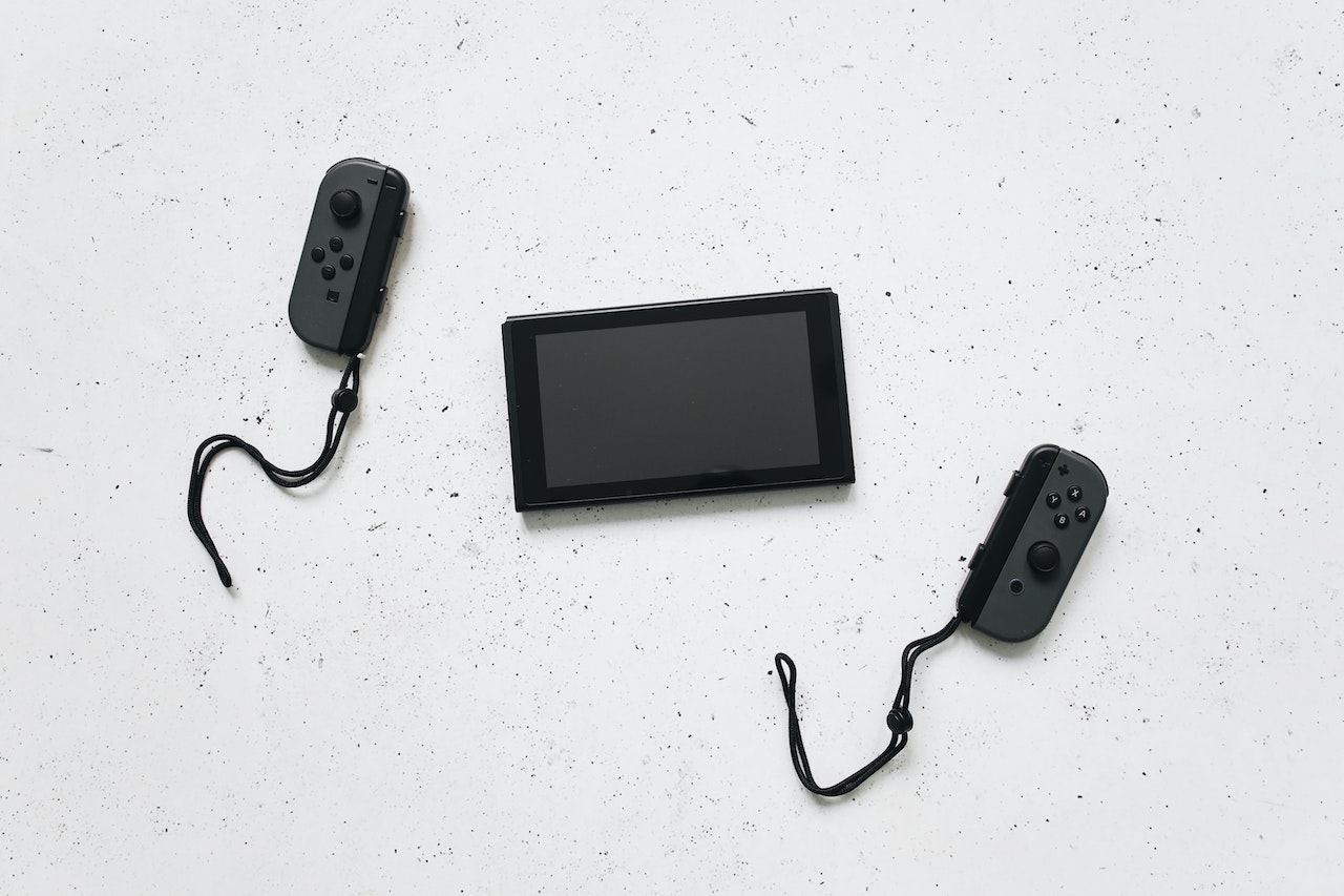 A Black Nintendo Switch near two black and gray JoyCon on top of a white surface