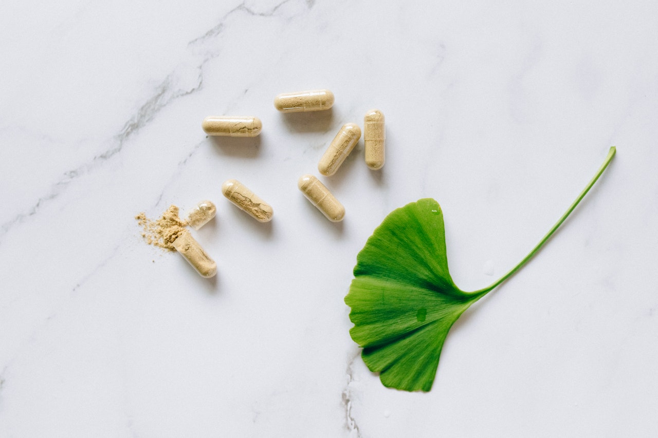 A Yellow colored supplement on a clear capsule near a green leaf on top of a white surface