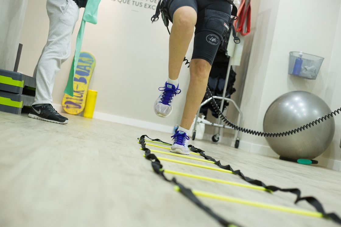 Man with running shoes skipping over a workout tool while his trainer looks on