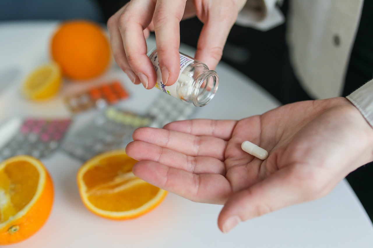 A person holding a clear medicine bottle and white capsule near the white table