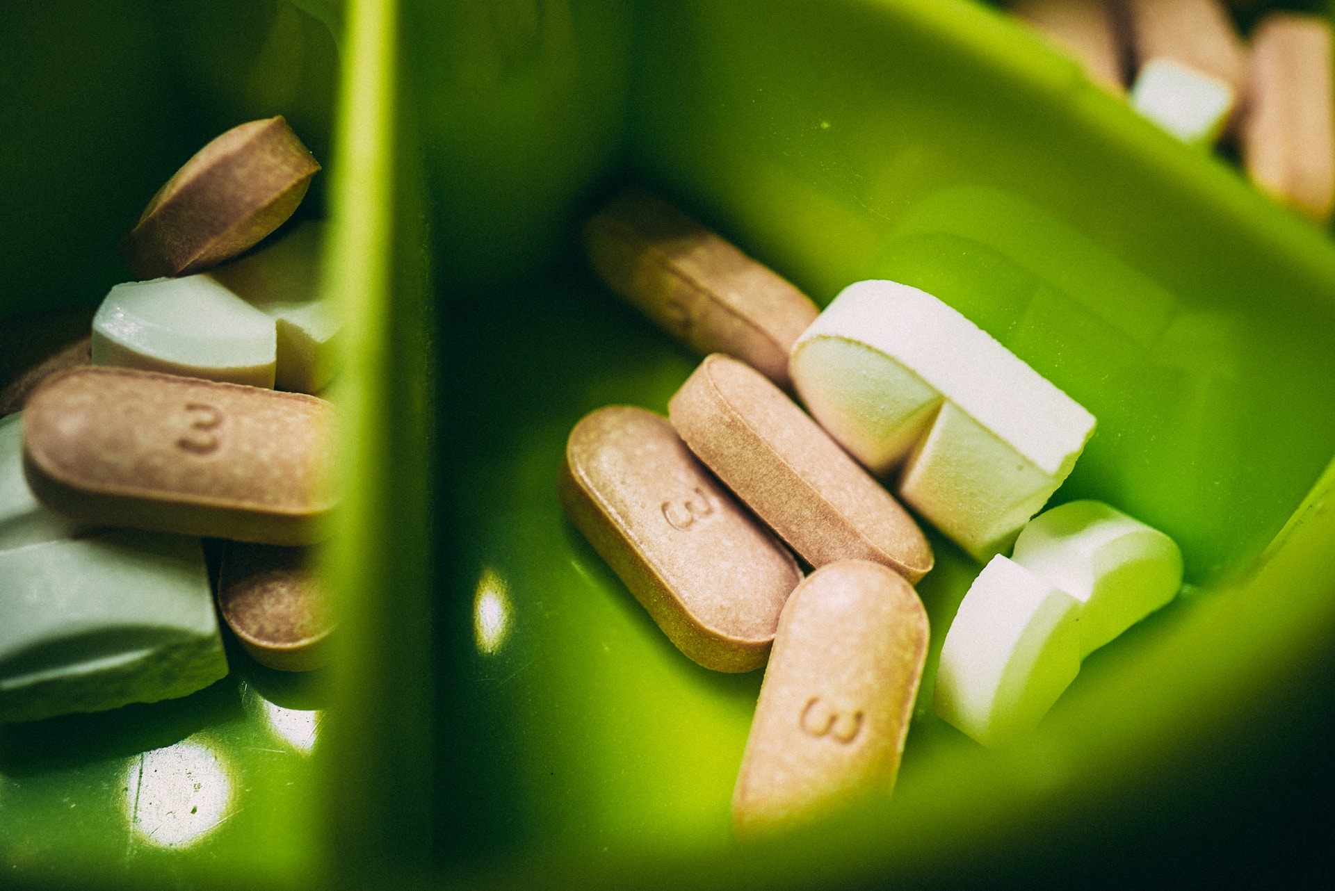 A white pill near a brown pill on a green medicine container