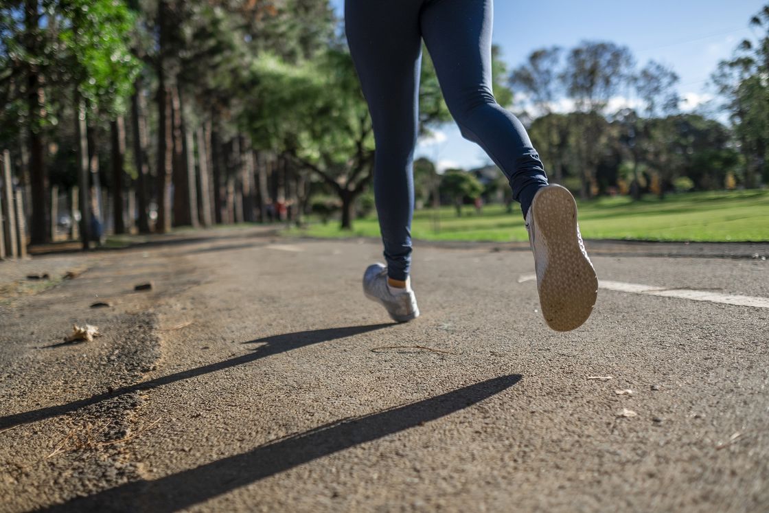 Woman wearing blue leggings and running on an empty pavement in a park