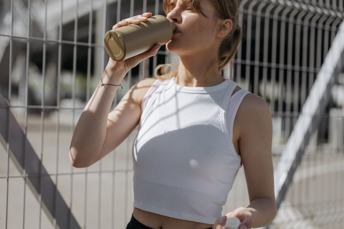 Woman drinking from her brown water bottle after running outdoors