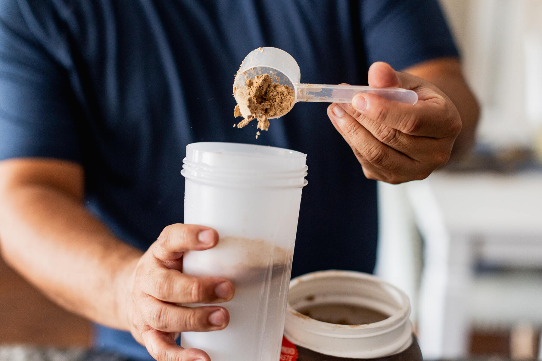 Man pouring a scoop of protein powder into a white bottle in the kitchen