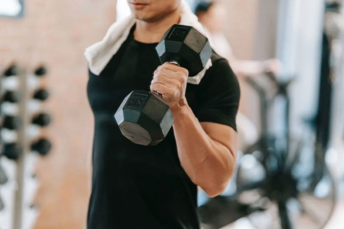 Person holding a black dumbbell with one arm during their exercise routine in a gym