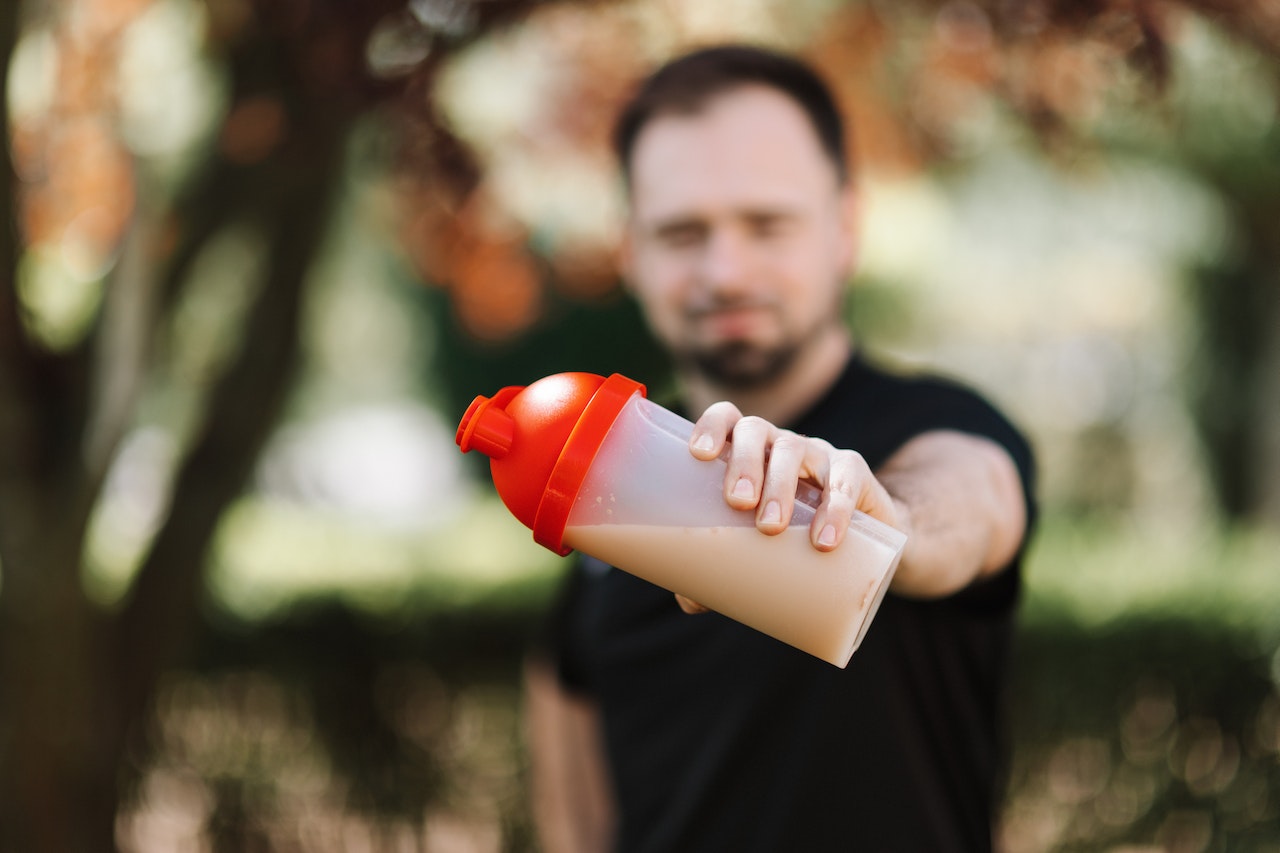 A man wearing a black shirt is holding a clear plastic tumbler with a red lid