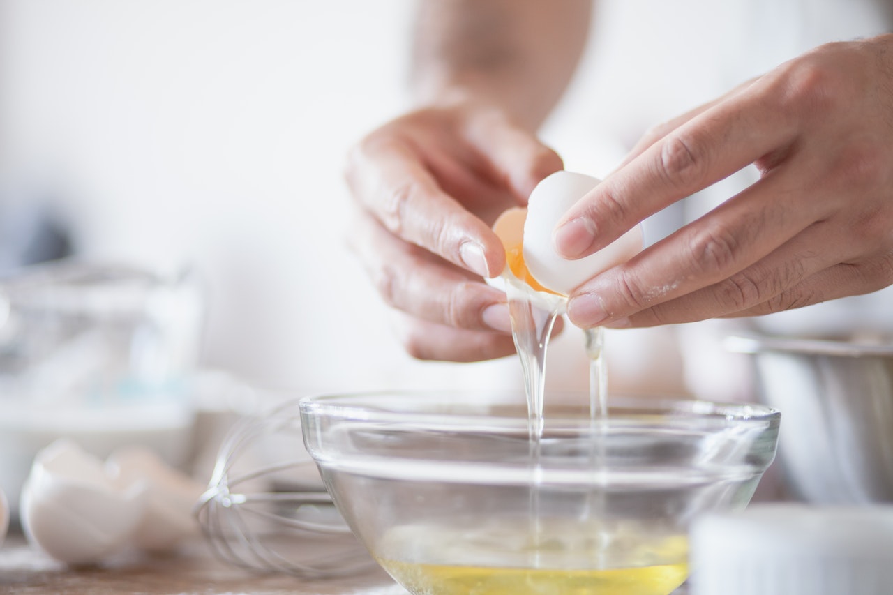 A person holding a white eggshell to separate the yolk from the egg white in a clear glass bowl