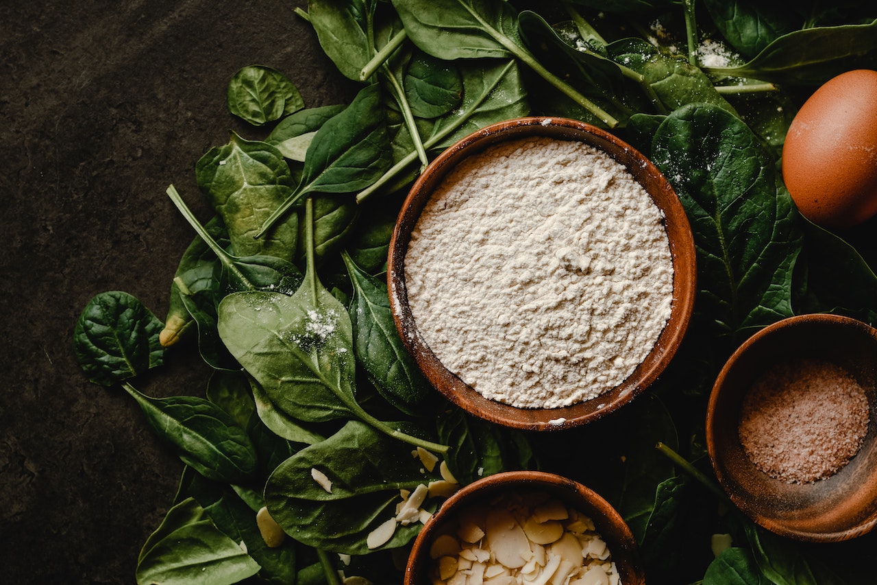 White flour on a brown wooden bowl on top of green leaves