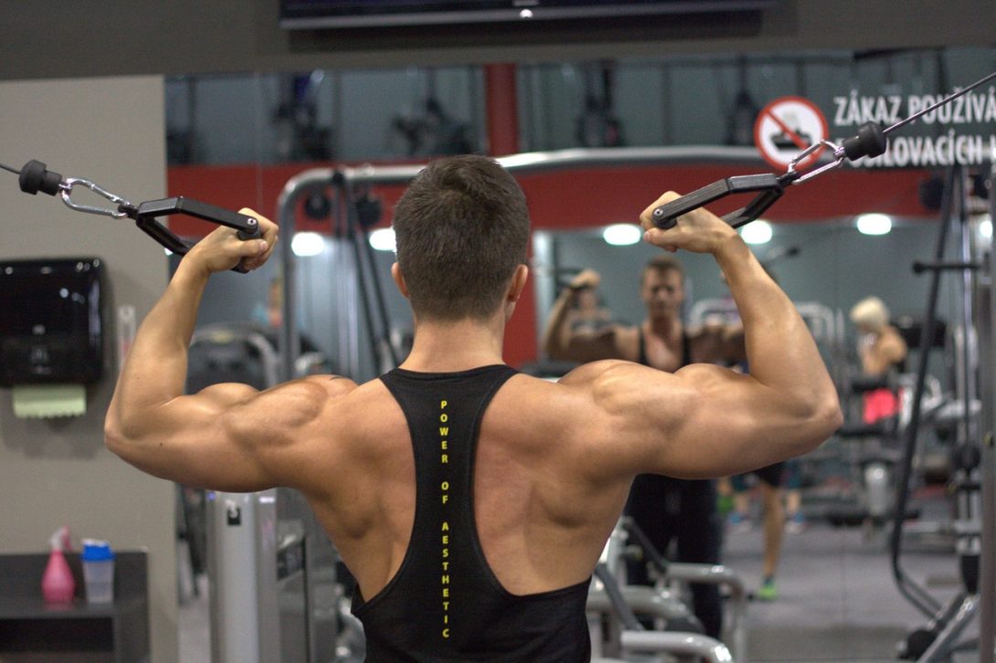 A man wearing a black tank top is using the black pull rope inside a well-lit gym.