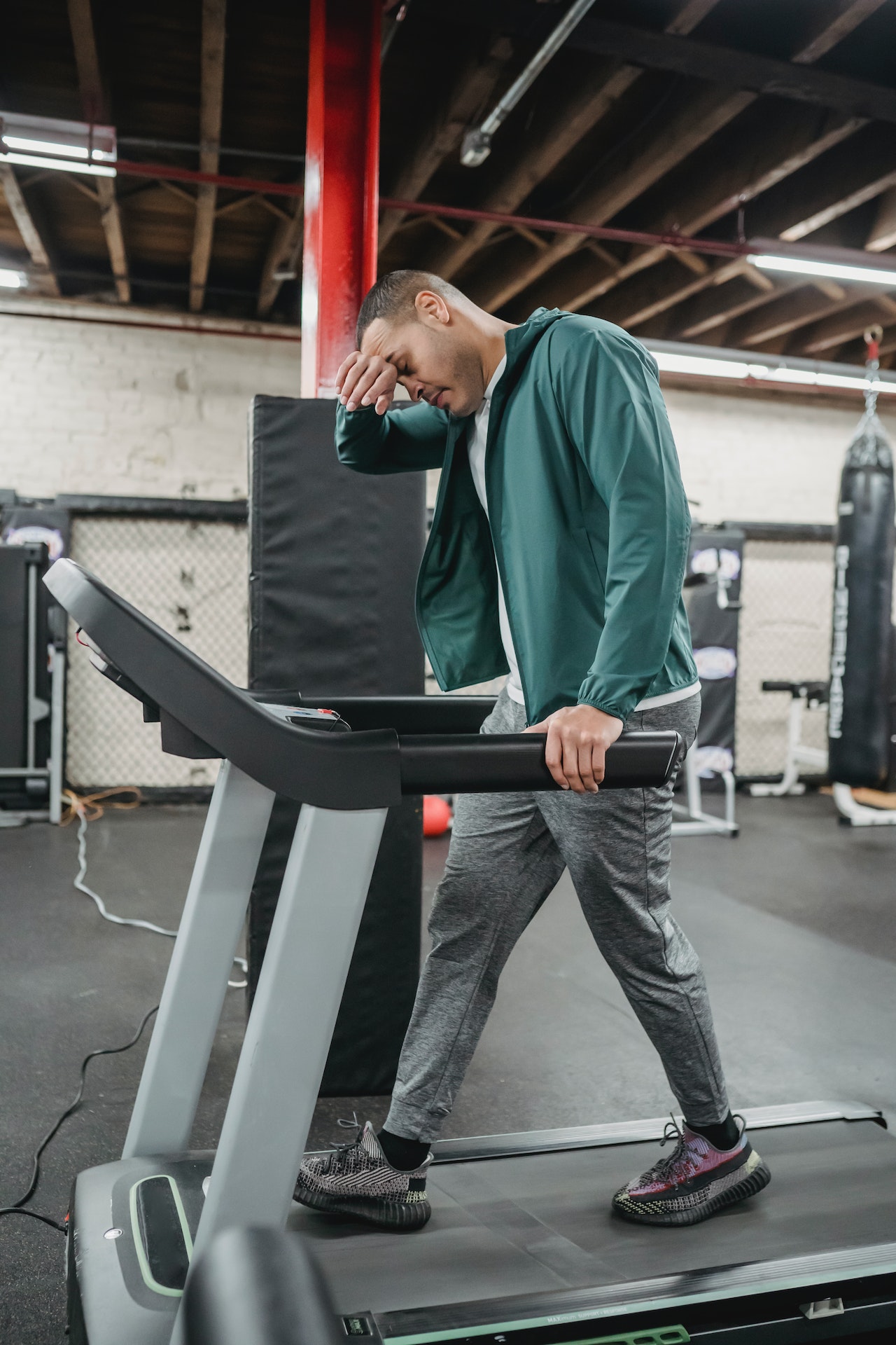 A man wearing a green jacket, white shirt, and gray pants is using the treadmill
