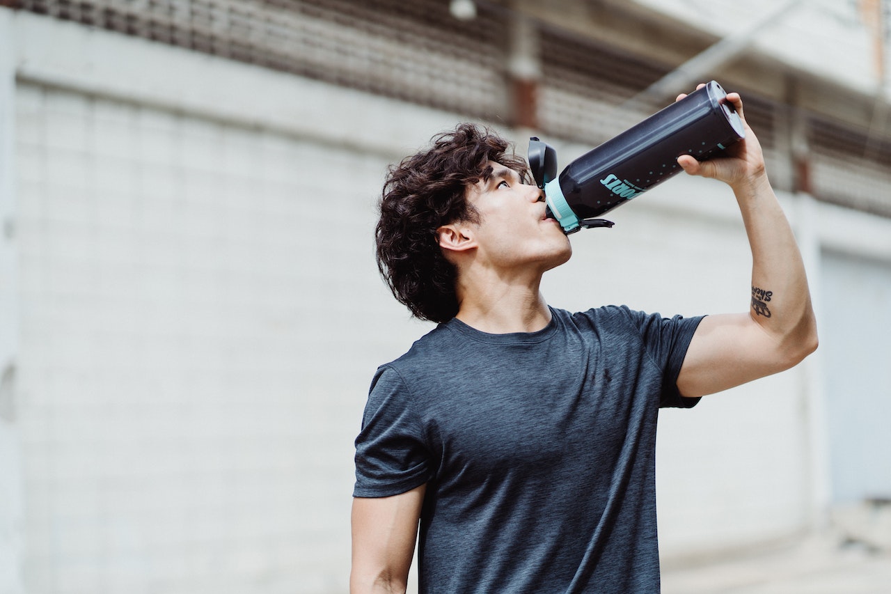 A man with curly hair is drinking from a black sports bottle with a blue lid