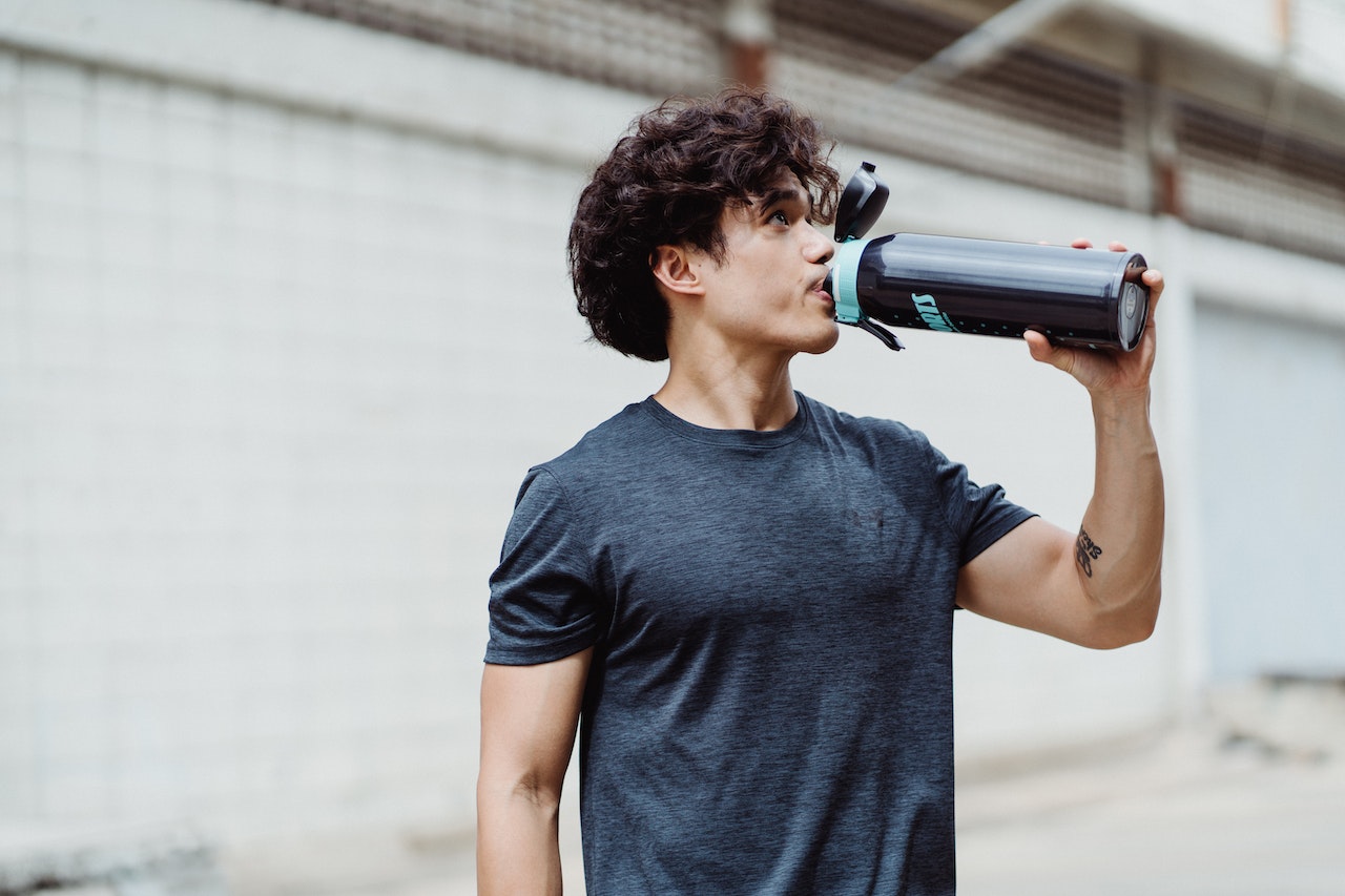 A man with curly hair is wearing a black shirt while drinking from a black sports bottle