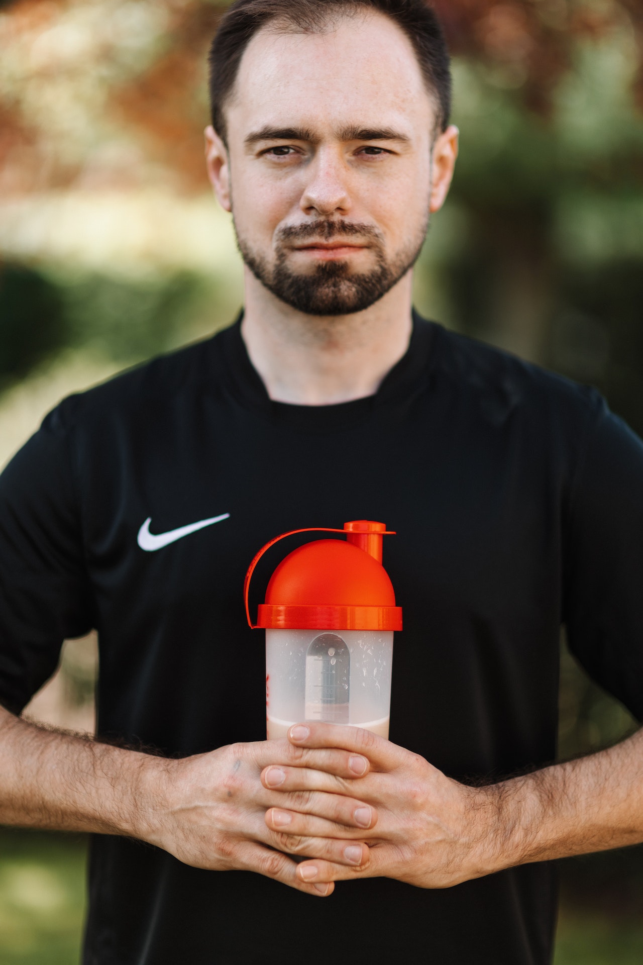 A man wearing a black Nike shirt is holding a clear plastic sports bottle with a red lid