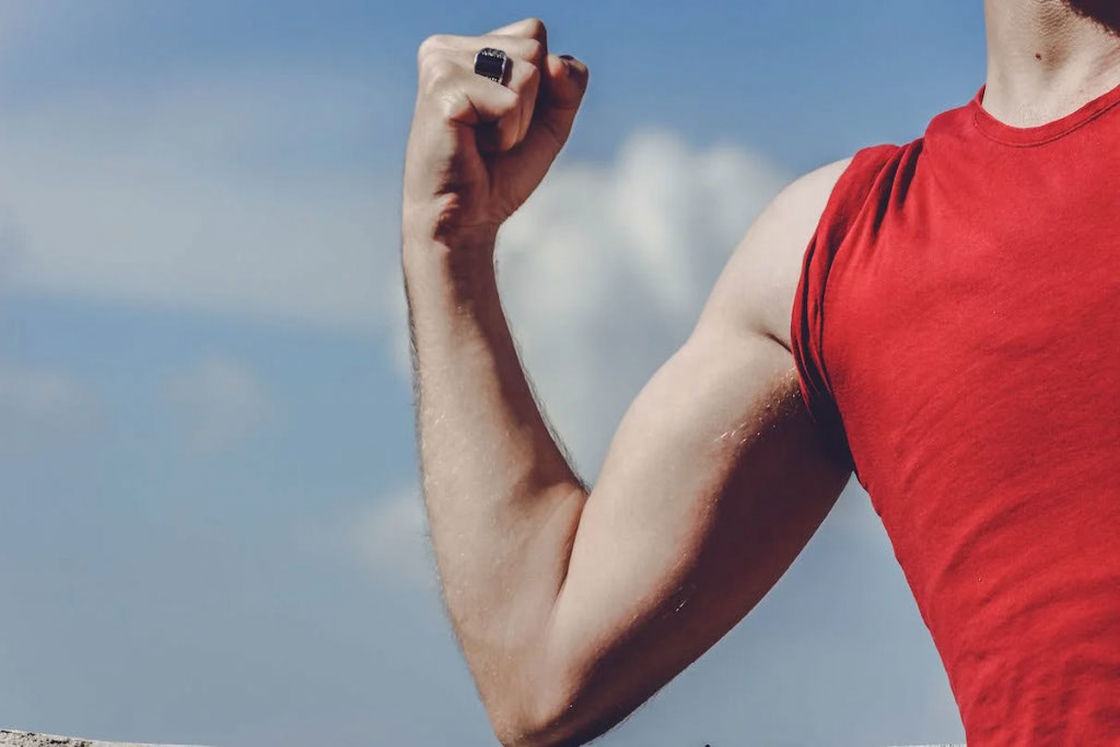Man wearing a red sleeveless shirt posing to show off his arm muscles