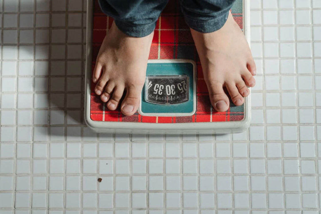 Person weighing himself on a red printed weighing scale in a tile bathroom floor