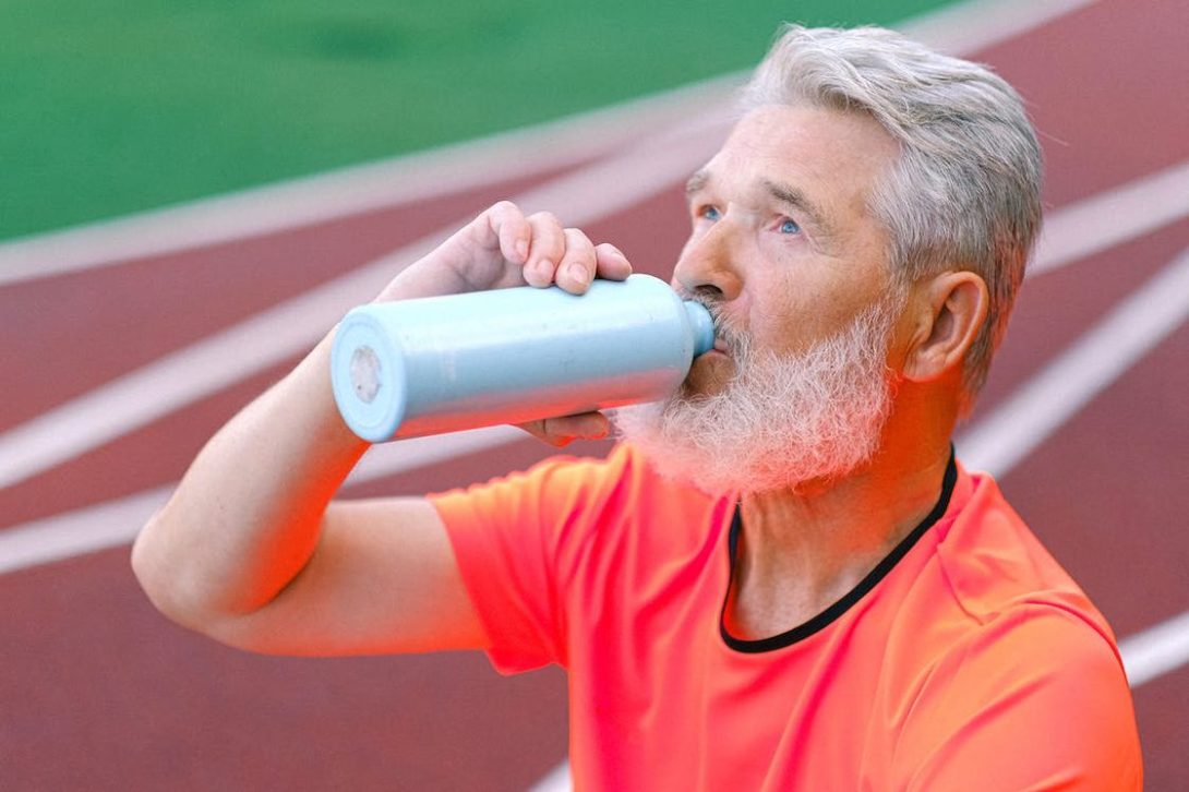 Man sitting on a track field while drinking from his blue aluminum bottle