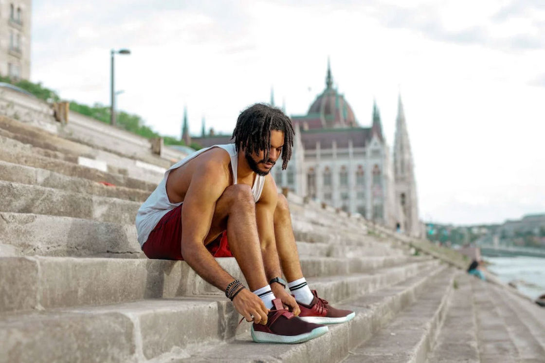 Man sitting on the concrete steps trying to tie his shoes before he goes for a run