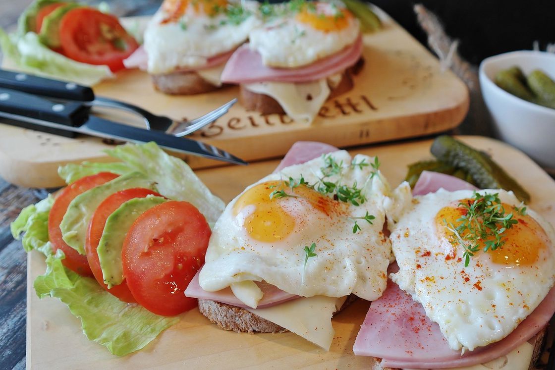 Open faced sandwiches placed on wooden boards with ham, cheese and eggs and tomato slices and lettuce on the side