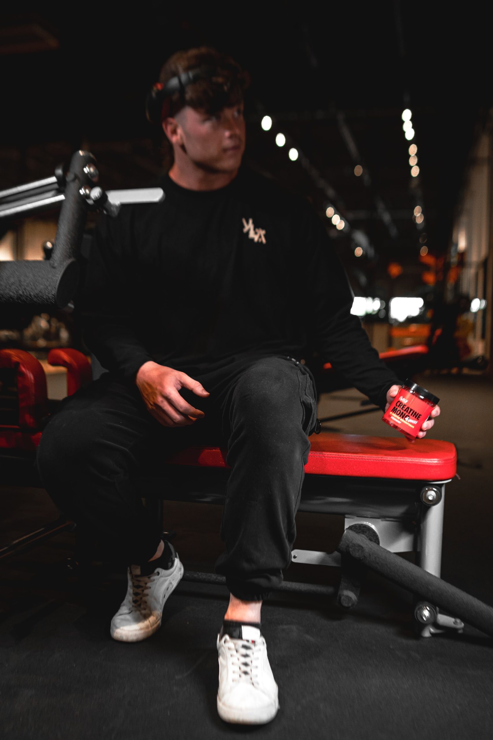 A man wearing black long sleeves and black pants is sitting on a red bench