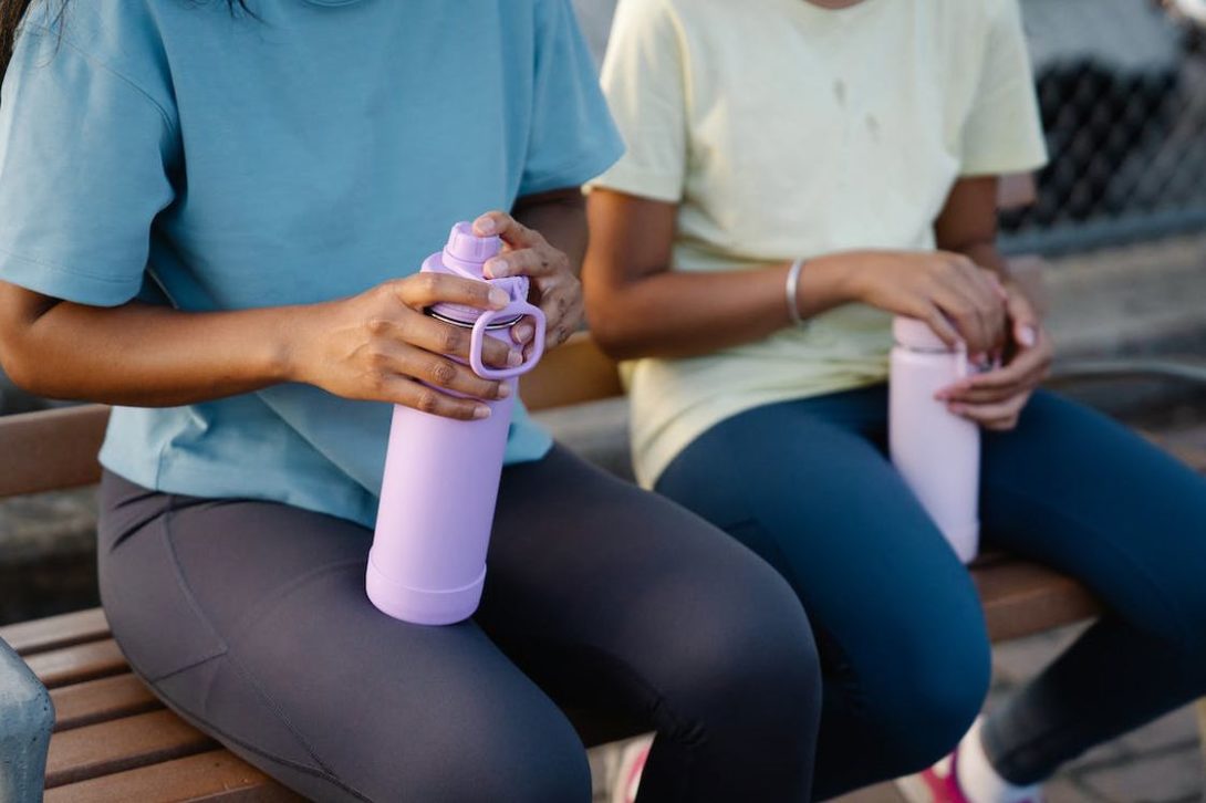 Two women sitting on a bench while holding their water bottles