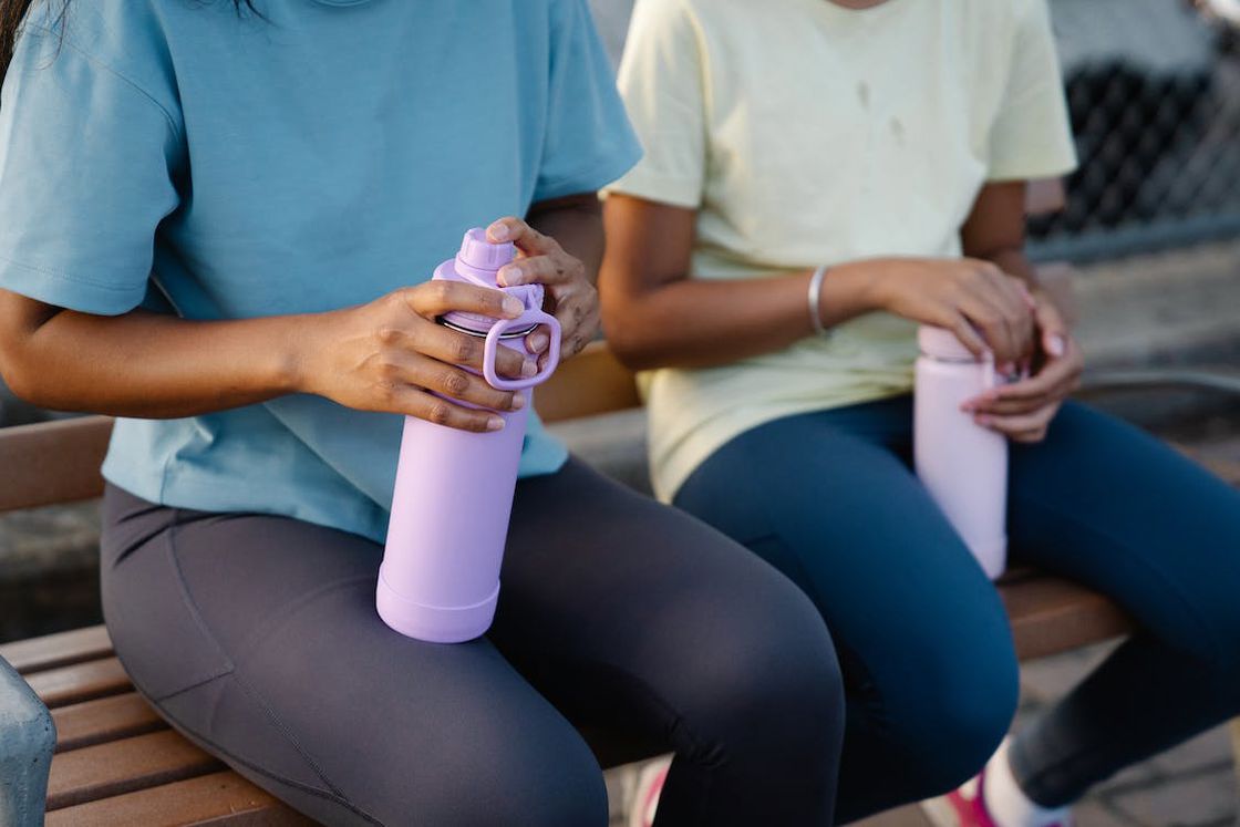 Two women sitting on a bench while holding their water bottles