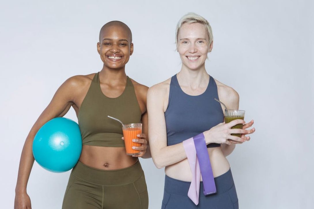 Two women in their athleisure both holding pre workout smoothies in a glass and steel straws