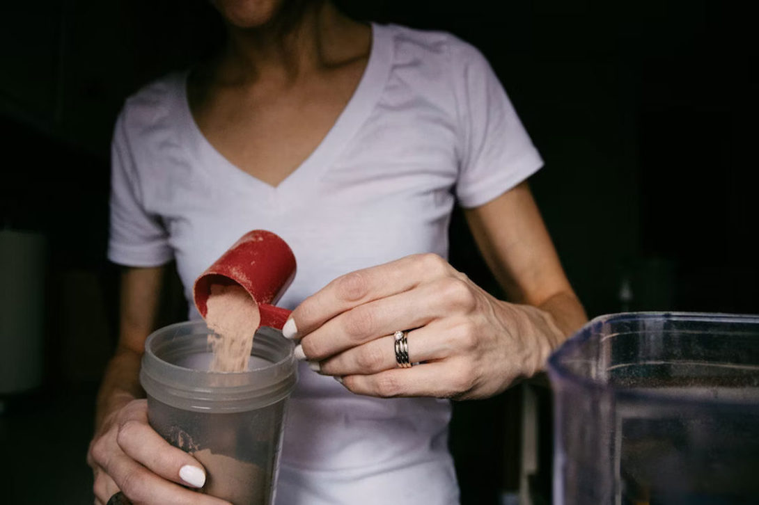 Woman pouring a scoop of supplement powder in a plastic tumbler