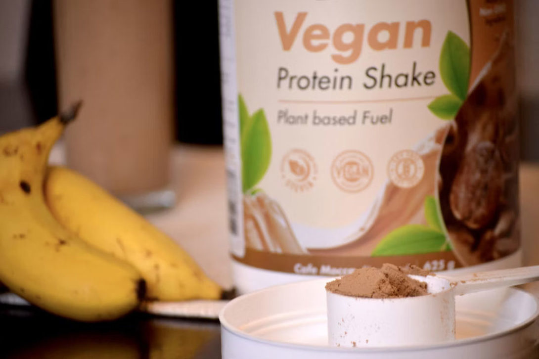 Scoop of chocolate vegan powder with a pair of bananas on the side