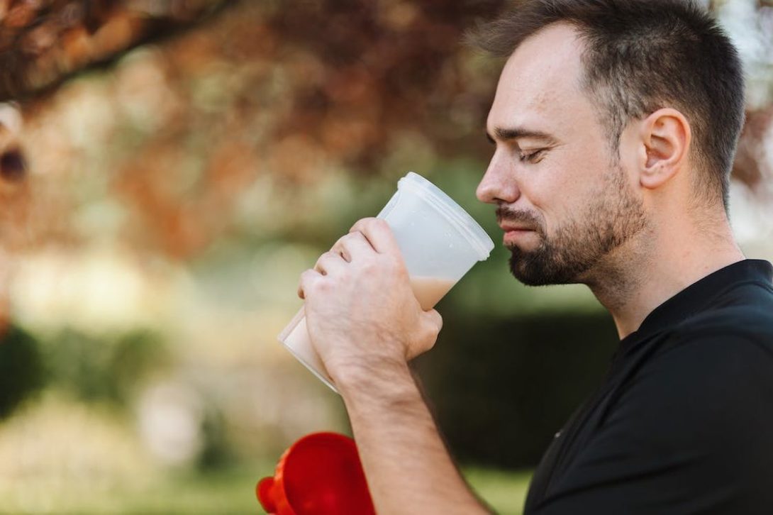 Man about to drink his protein supplement mix from a plastic tumbler while exercising outdoors