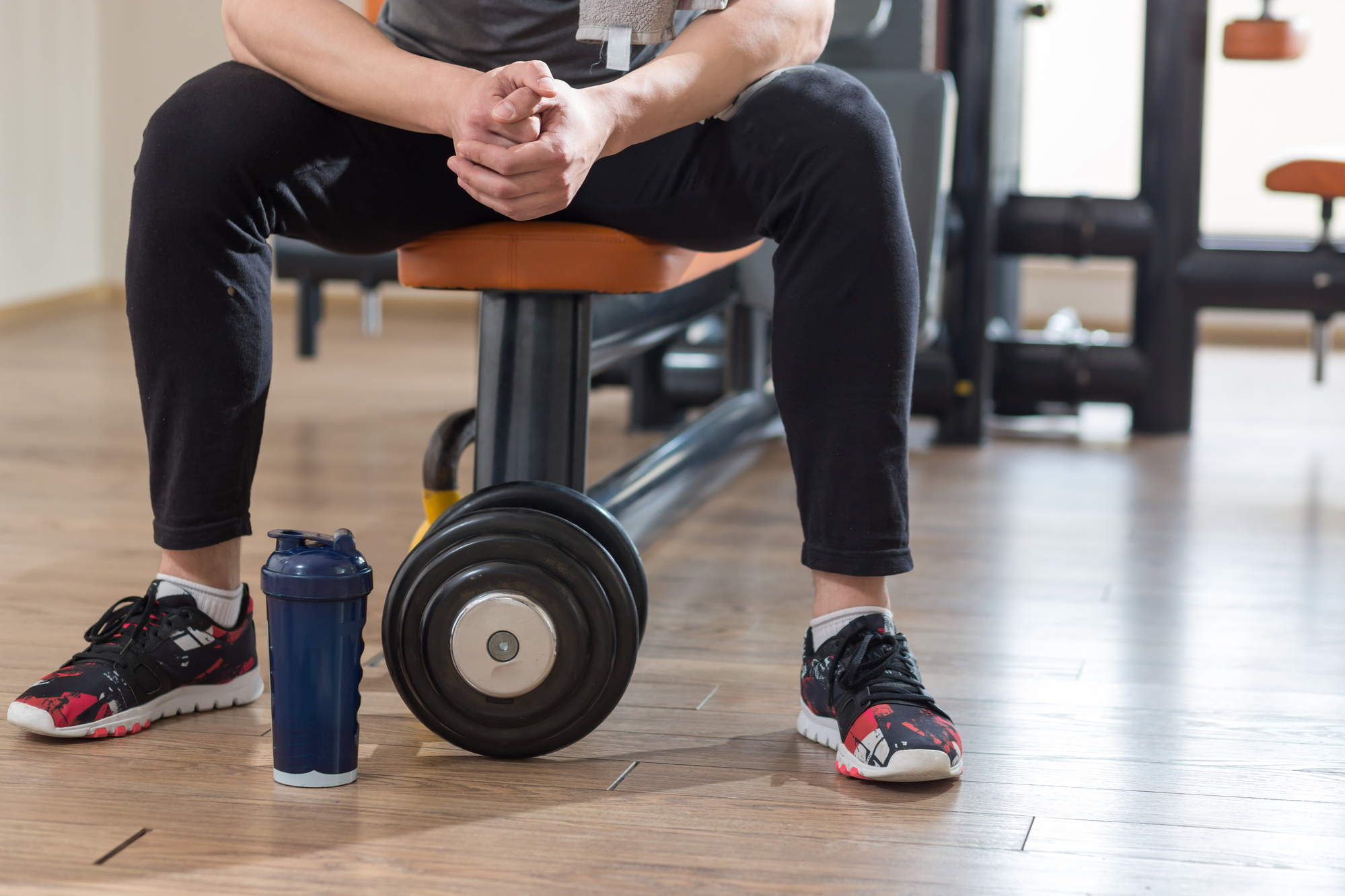 Man sitting on a workout bench with a blue water bottle next to his feet on the gym floor