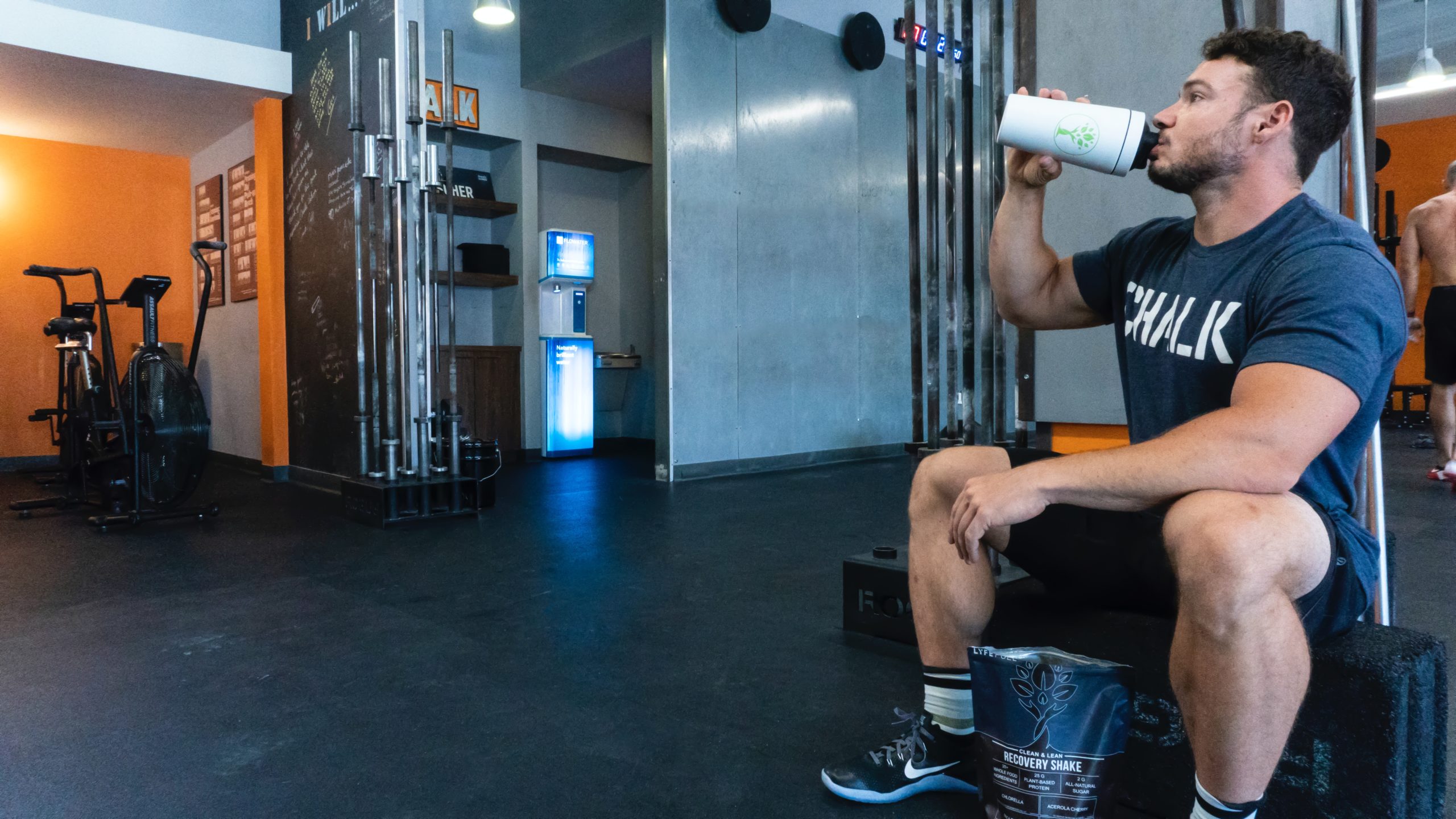 A man sitting and drinking on a white tumbler on the gym