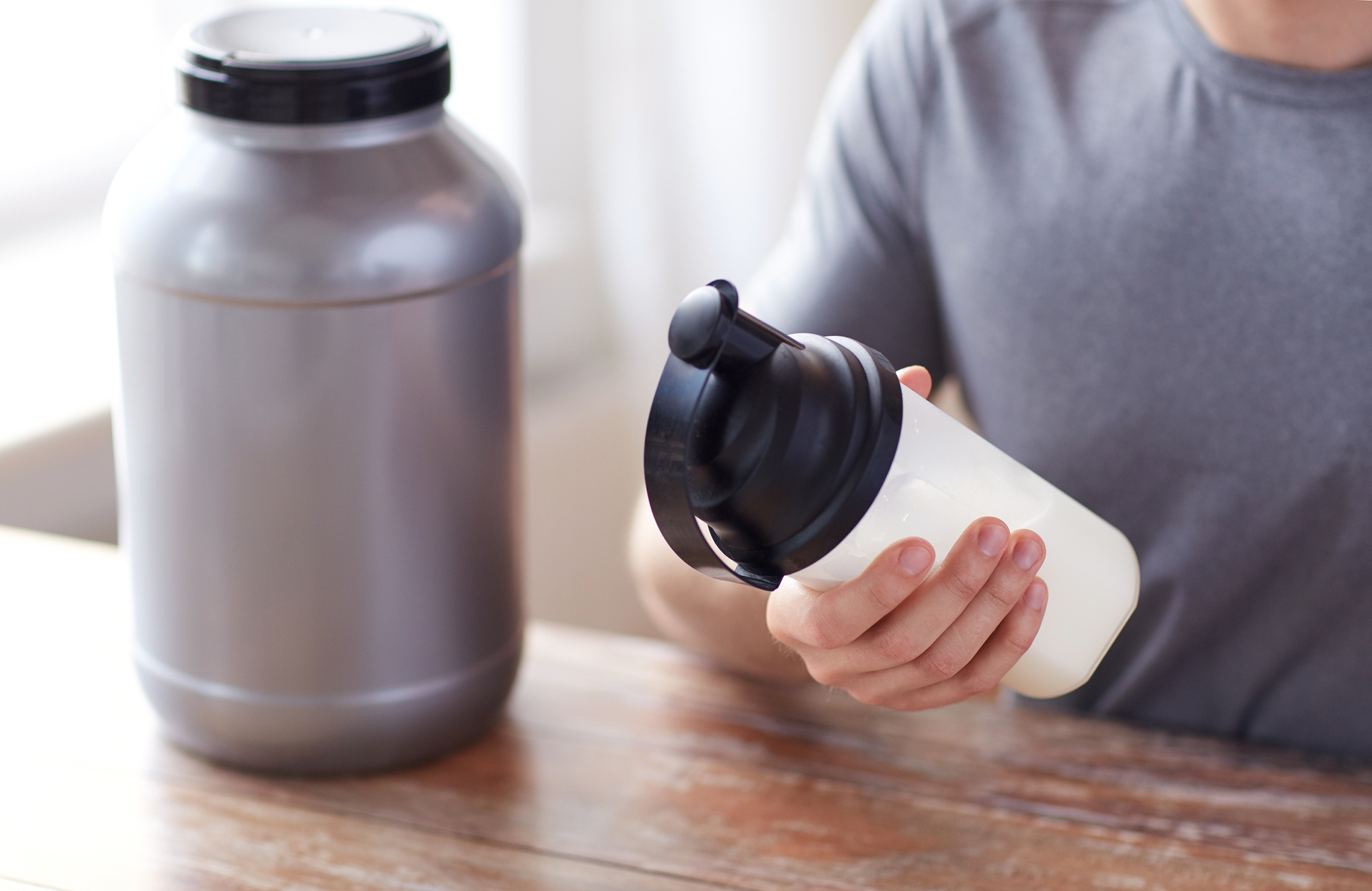 close up of man holding a protein shake bottle and gray container of pre-workout