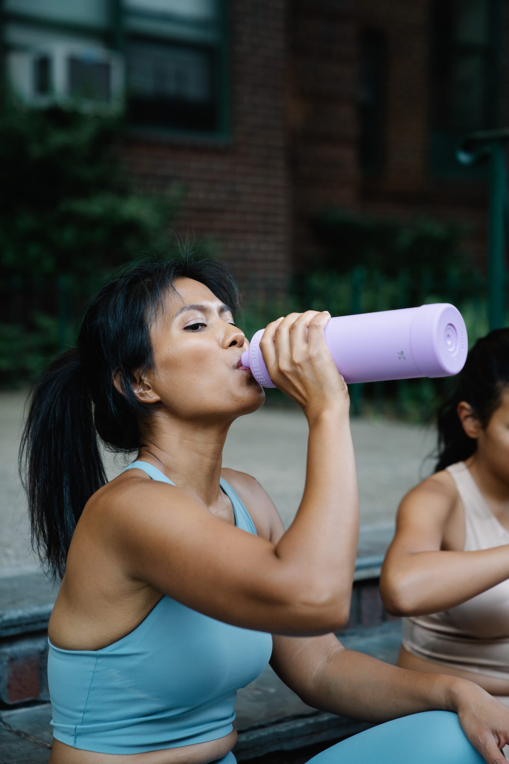 Woman in a blue workout outfit sitting and drinking pre workout from her purple water bottle