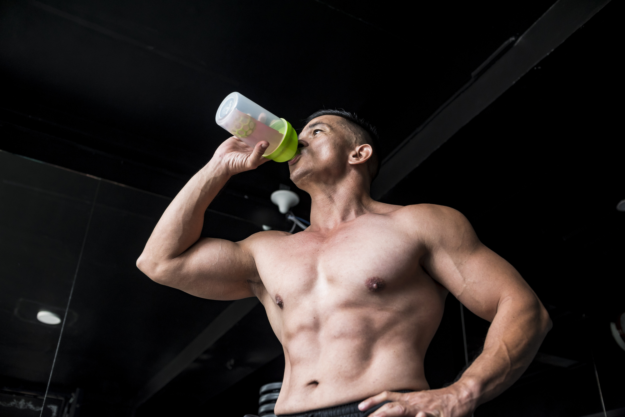 Fit man drinks his pre workout drink from a green water bottle in a gym