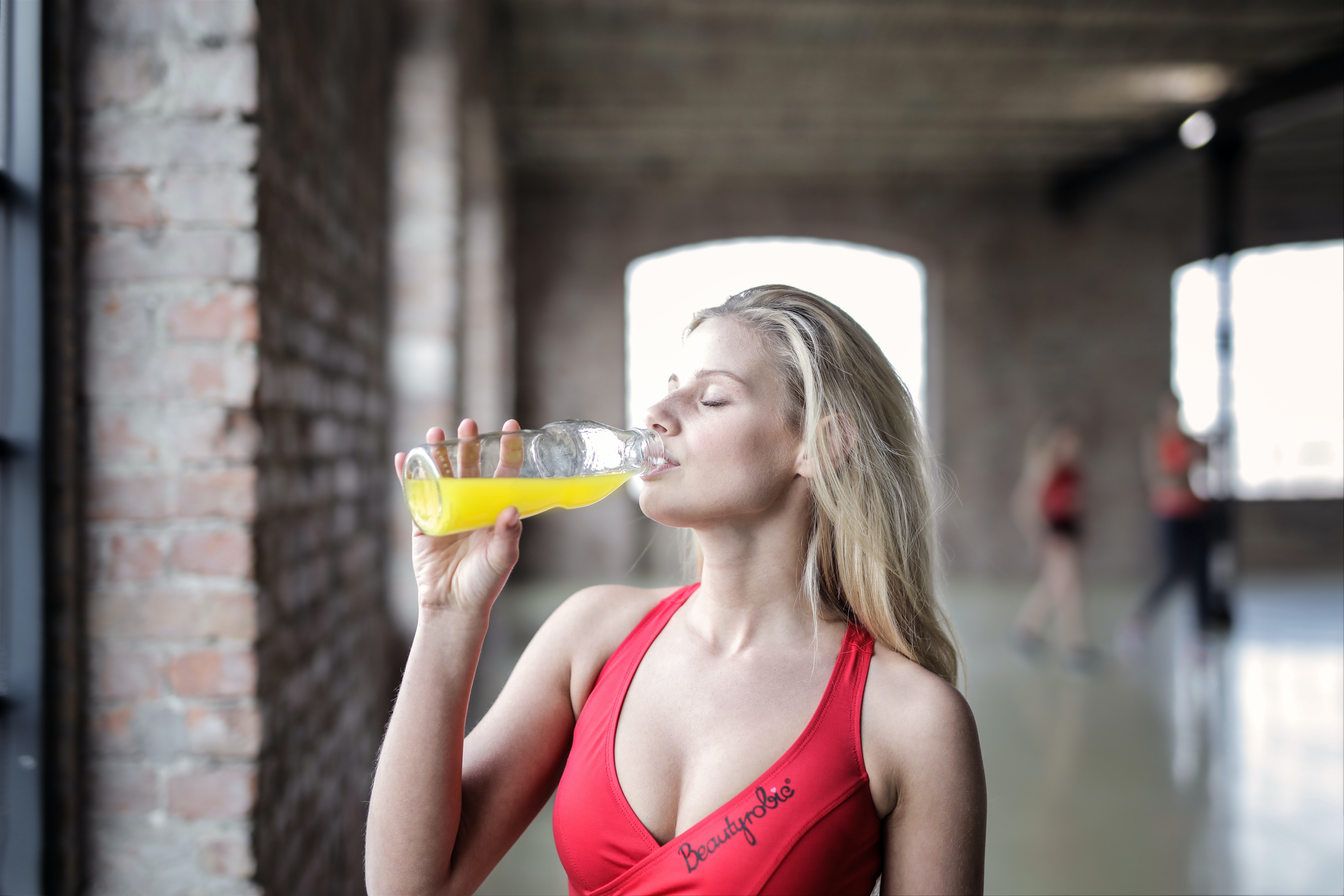 A man wearing a sports bra drinking a yellow beverage
