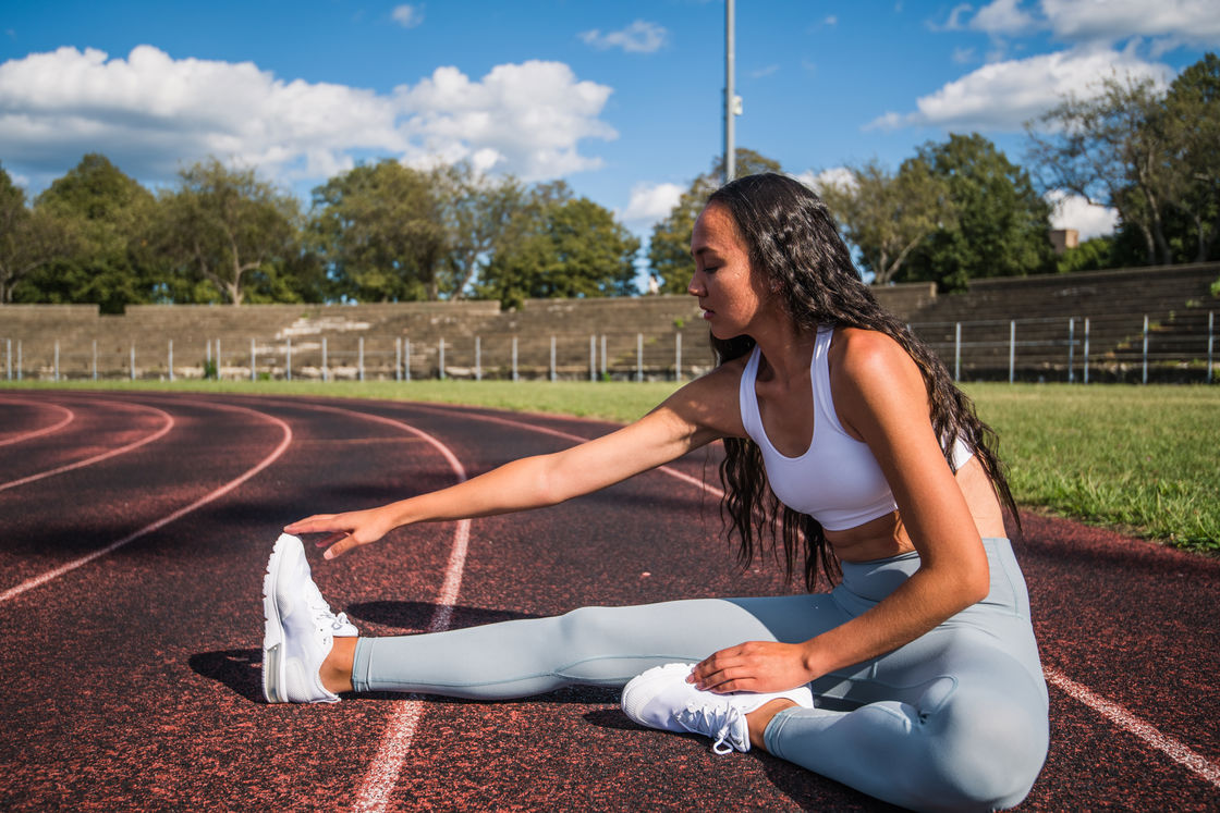 Woman stretching her legs on an outdoor field track