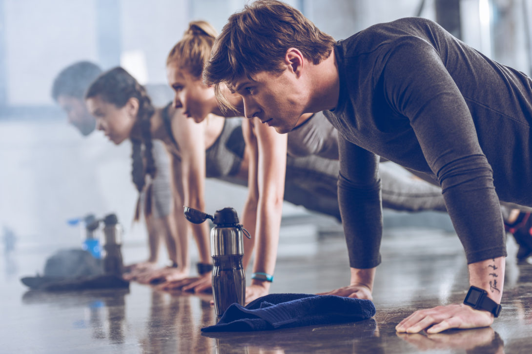 Group of men and women in a pushup position on a gym floor with water bottles next to them
