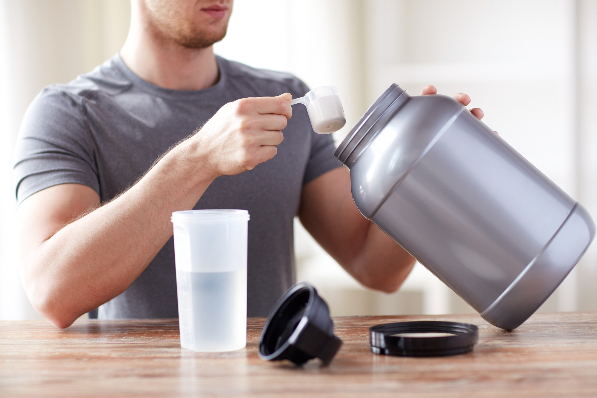 Man holding creatine about to pour it into a bottle on a wooden table