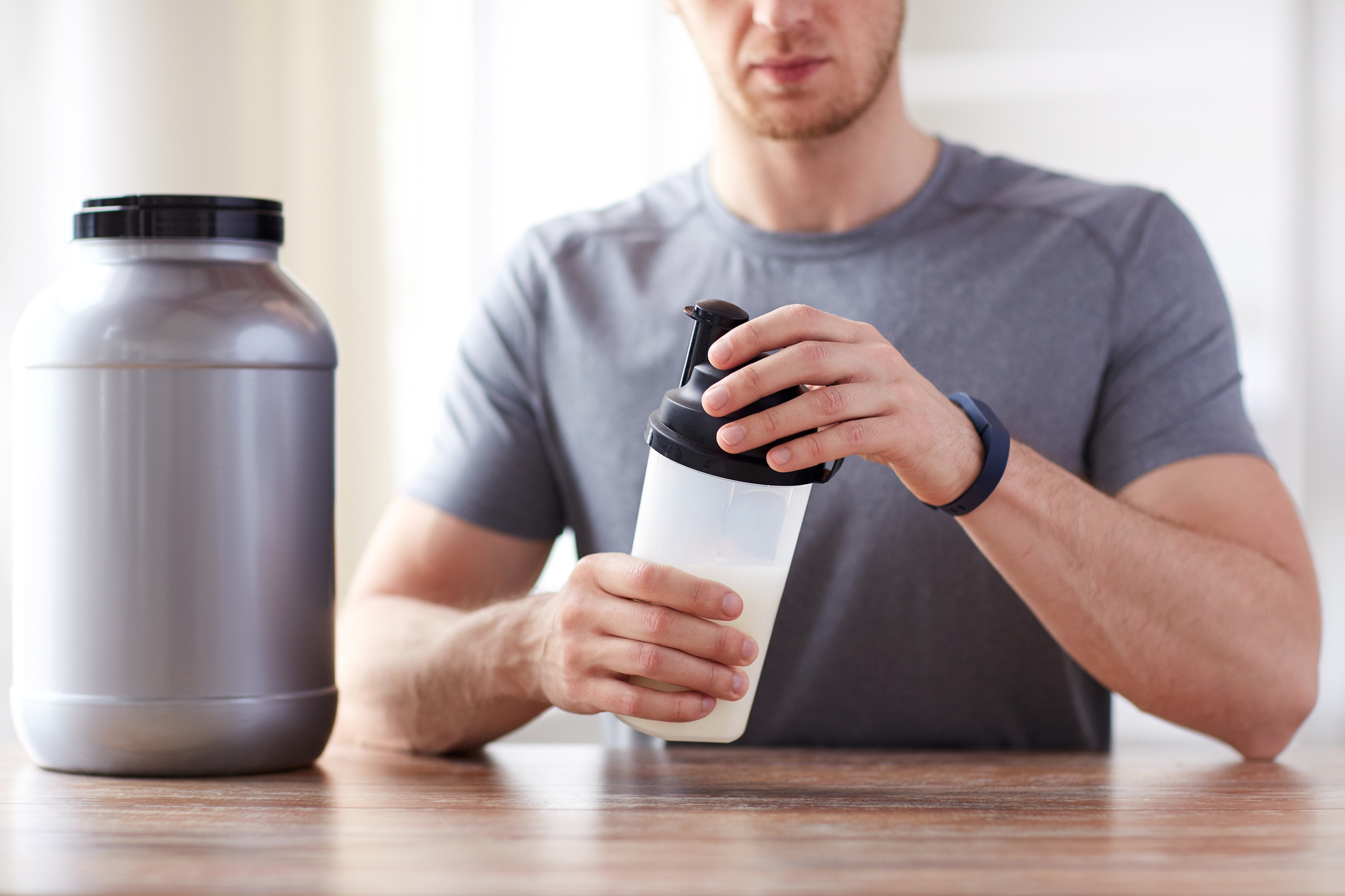 Man holding his shaker bottle with a jar of creatine next to him on a wooden table