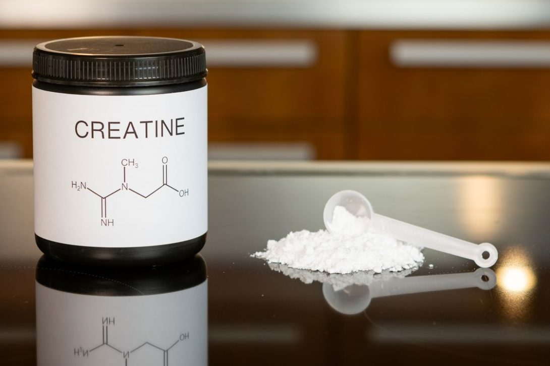 Creatine bottle with a scoopful of white creatine powder on the table