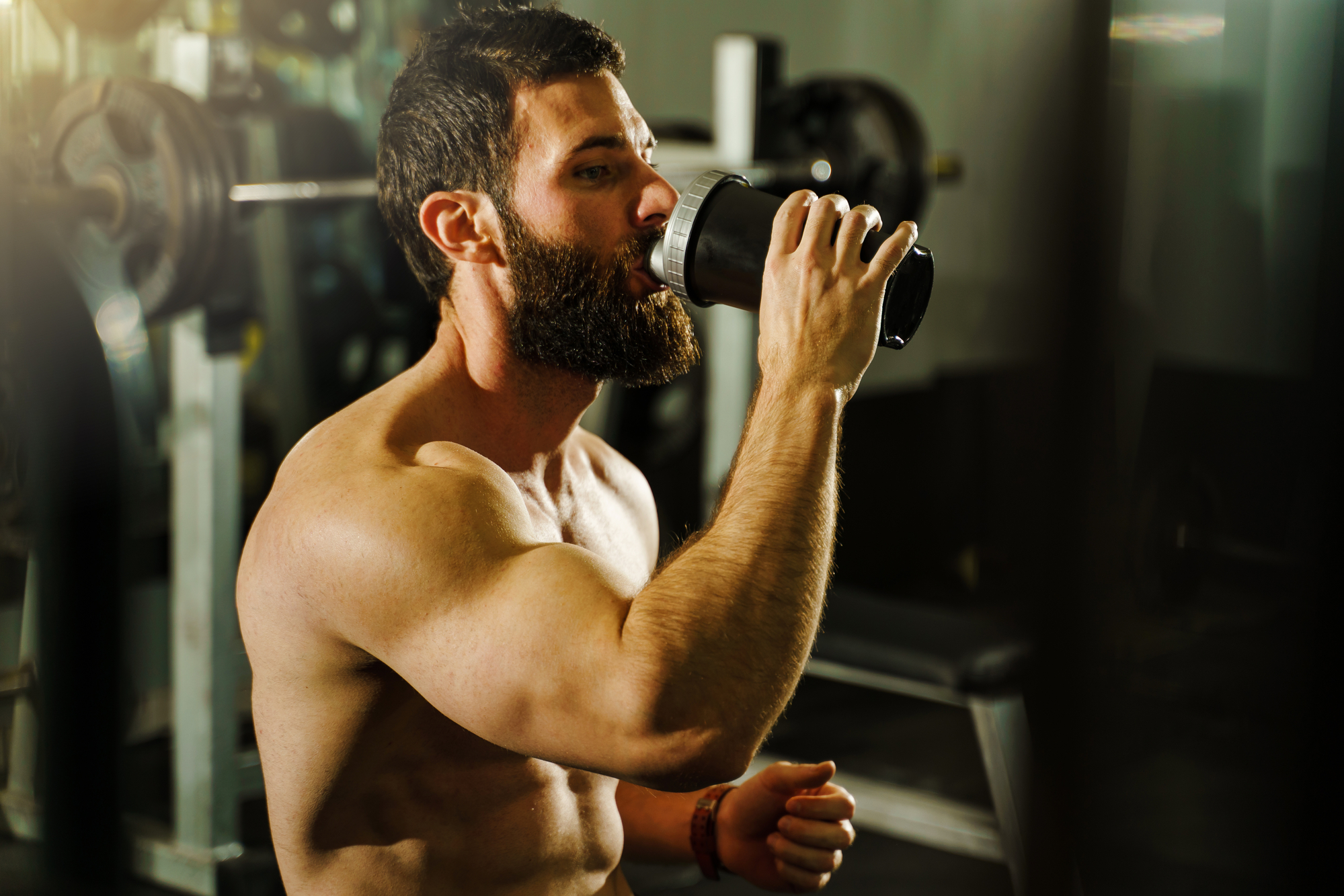 Fit man sitting by exercise equipment drinking from his black waterbottle