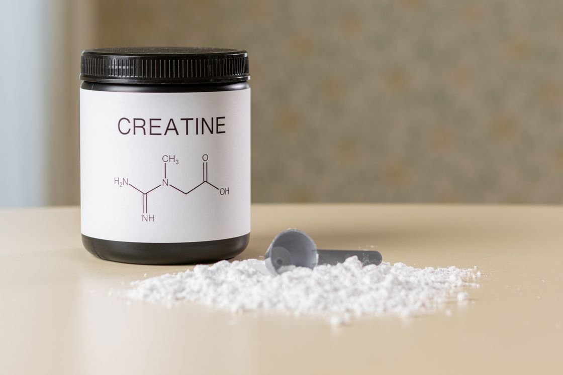 Creatine bottle with a scooper and white powder on the table