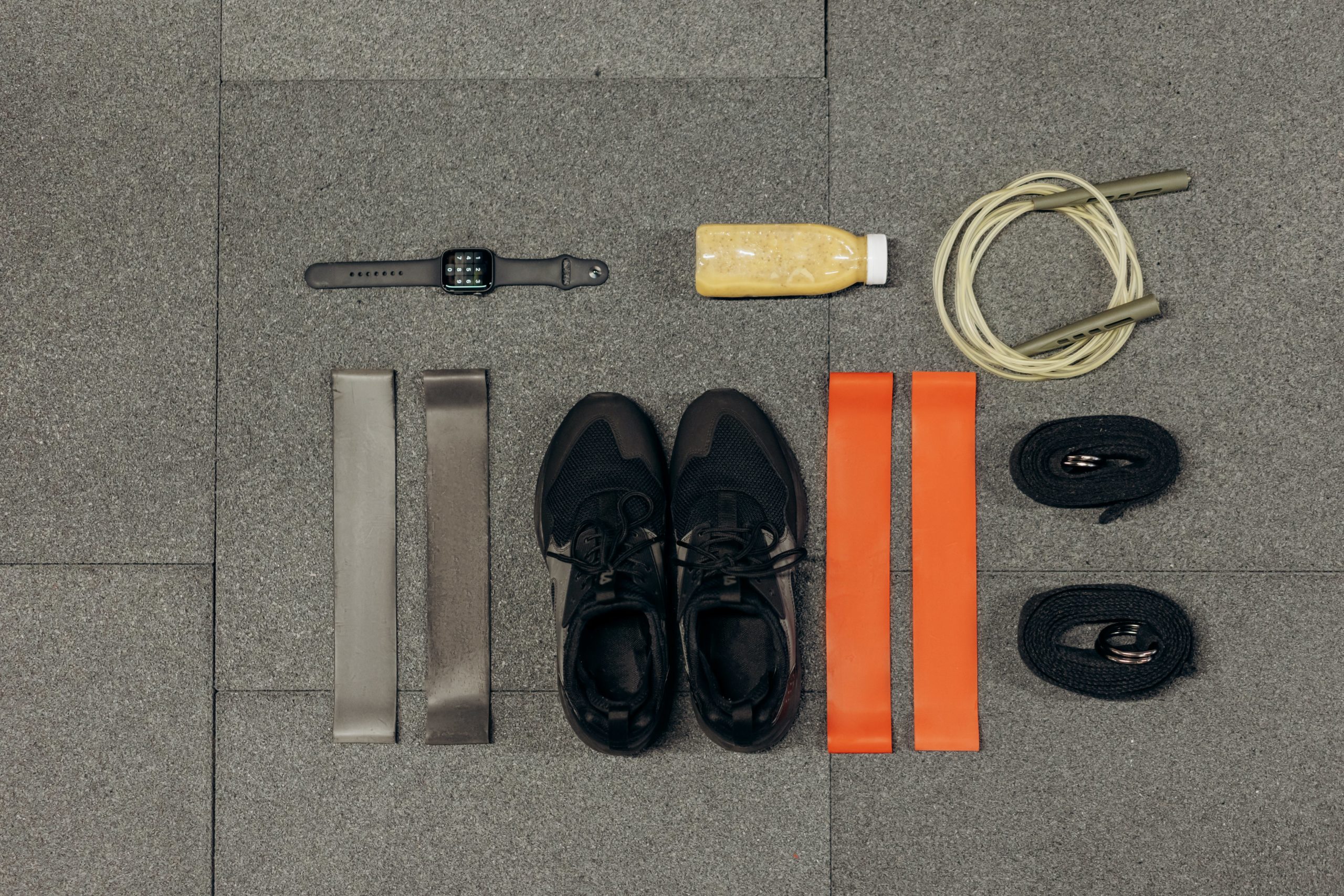 Workout tools like bands, shoes, watch, drinks, and jumping rope placed on the ground