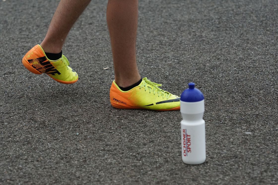 Close up of a man wearing soccer cleats while a white sports bottle is placed on the ground