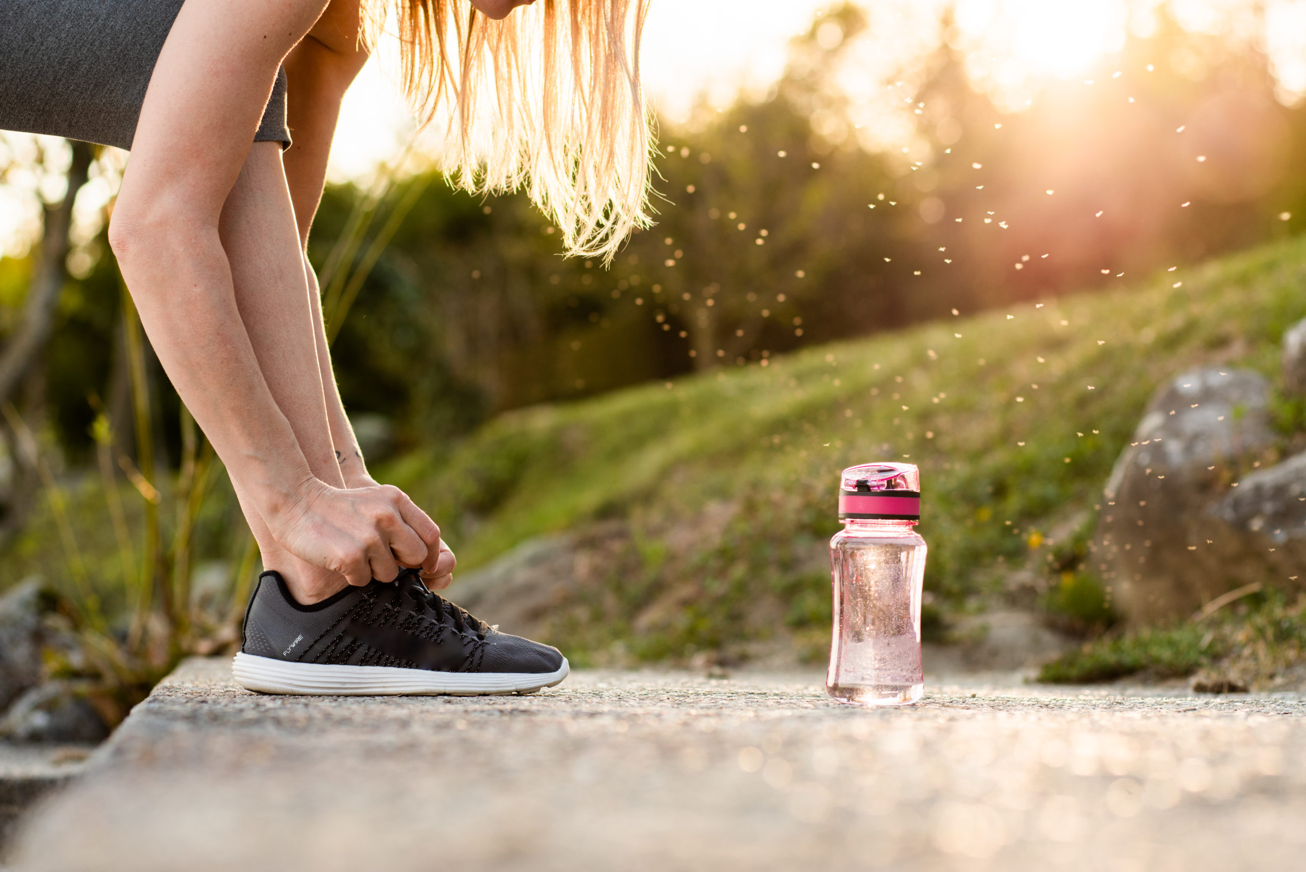 A woman tying her shoe laces with a pink water tumbler in front of her