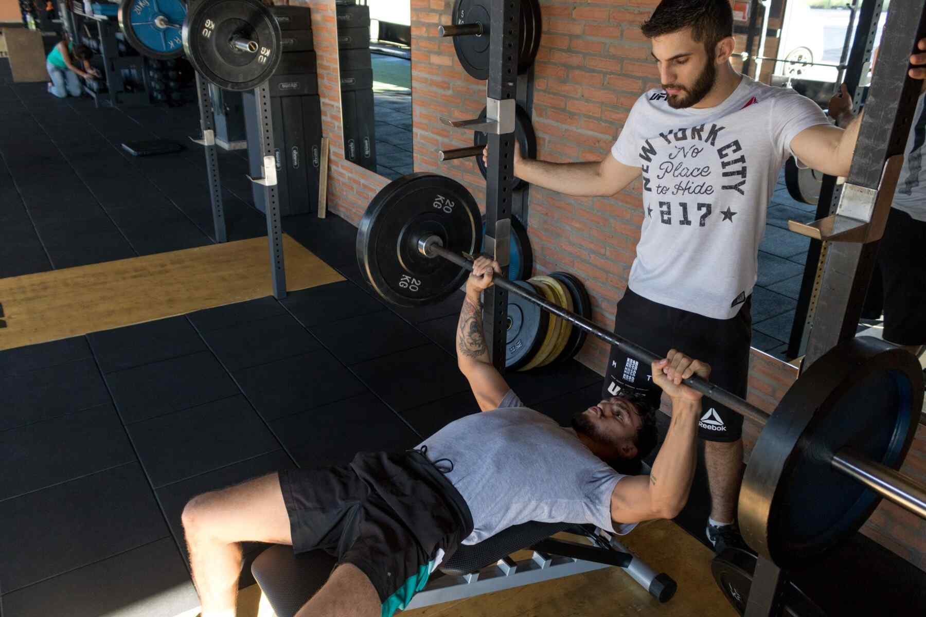 A man assisting another man while lifting a barbell