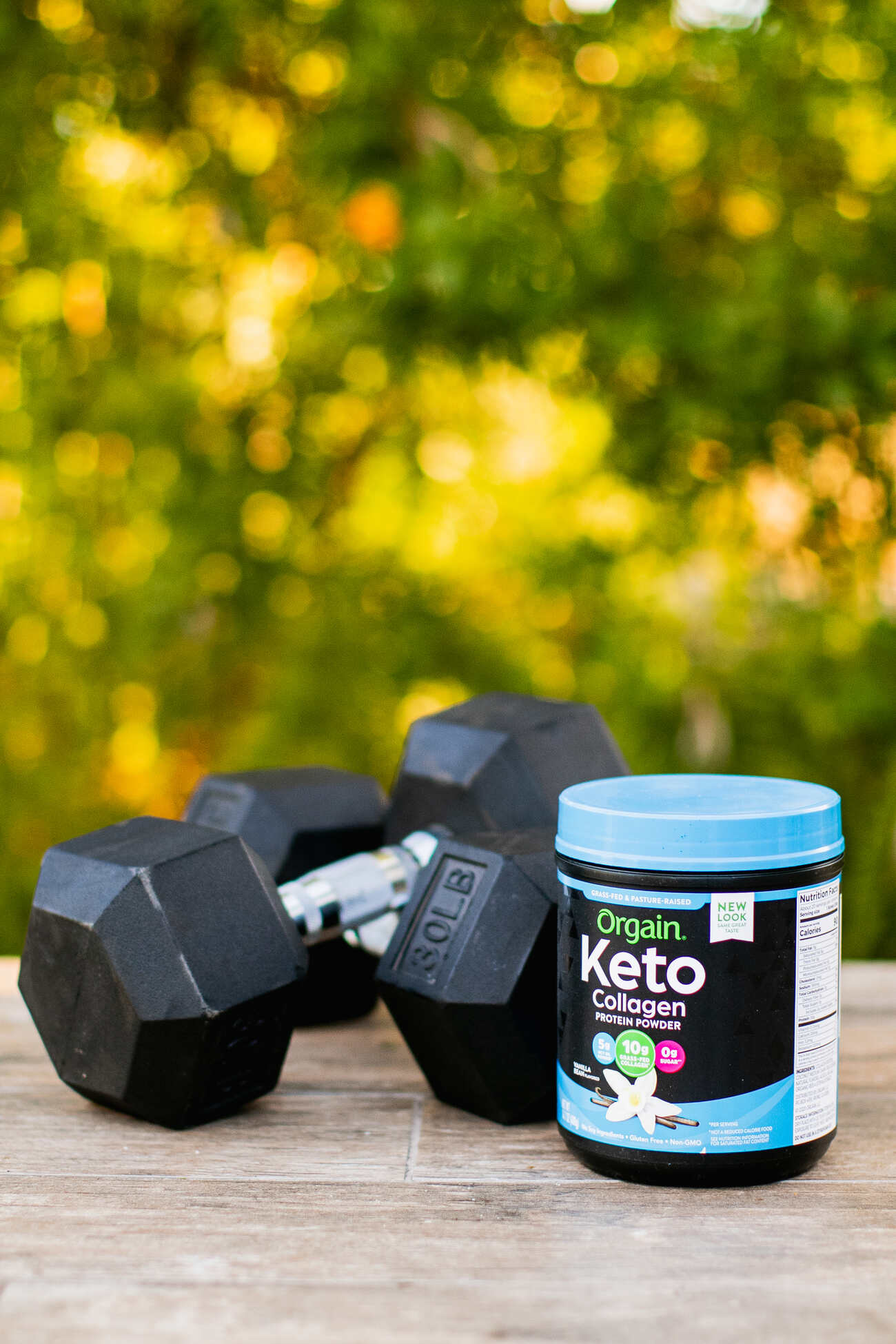 Orgain Keto Collagen container next to 30lb dumbbells on a wooden table outside