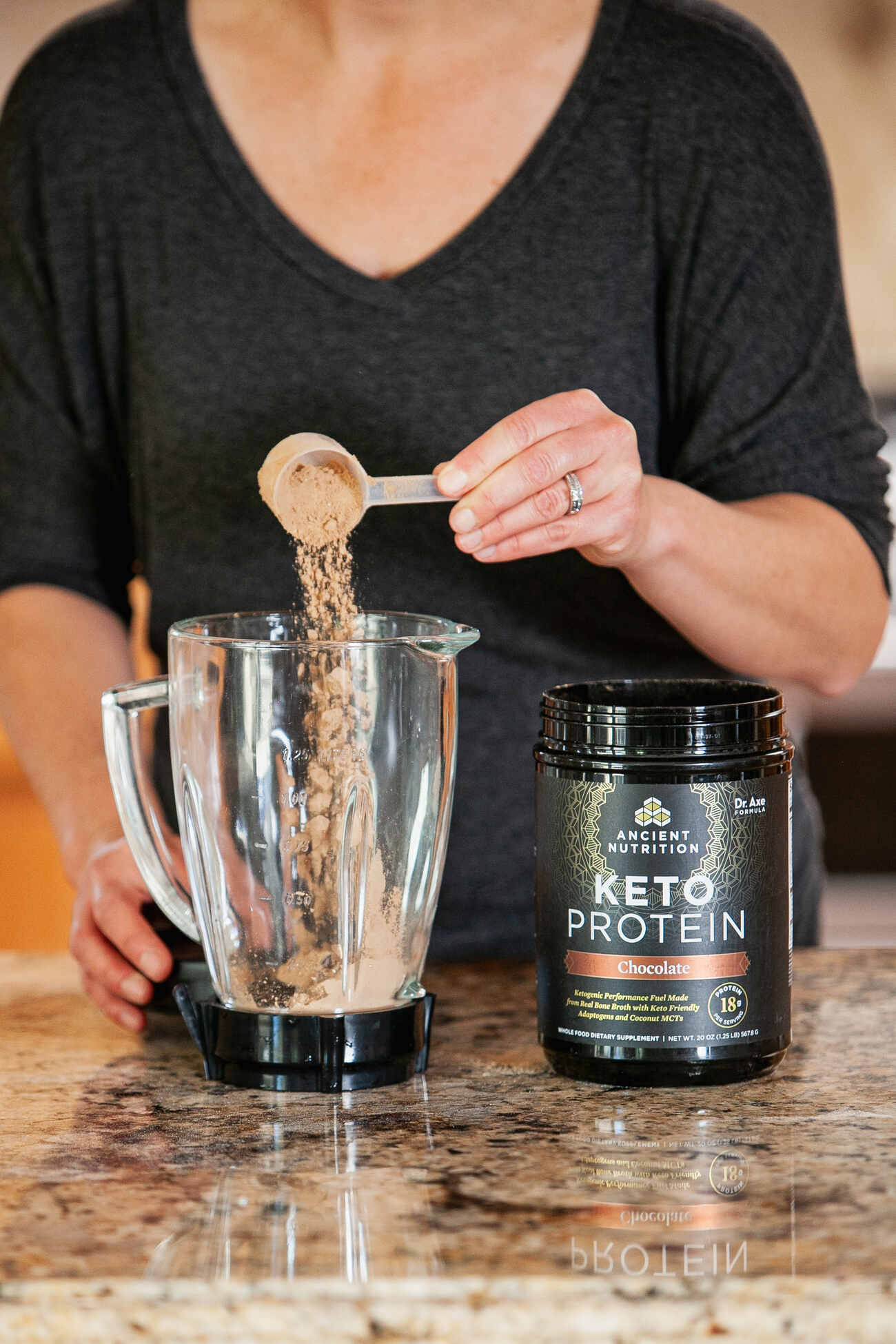 Woman pouring chocolate keto protein powder from Ancient Nutrition into a glass blender