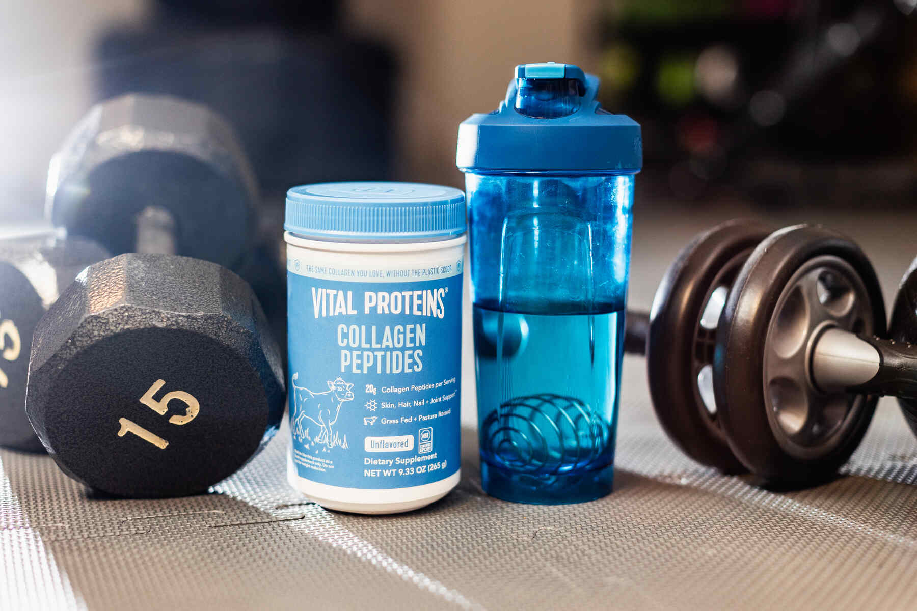 Vital Proteins Collagen peptides beside a water tumbler and a pair of dumbbells