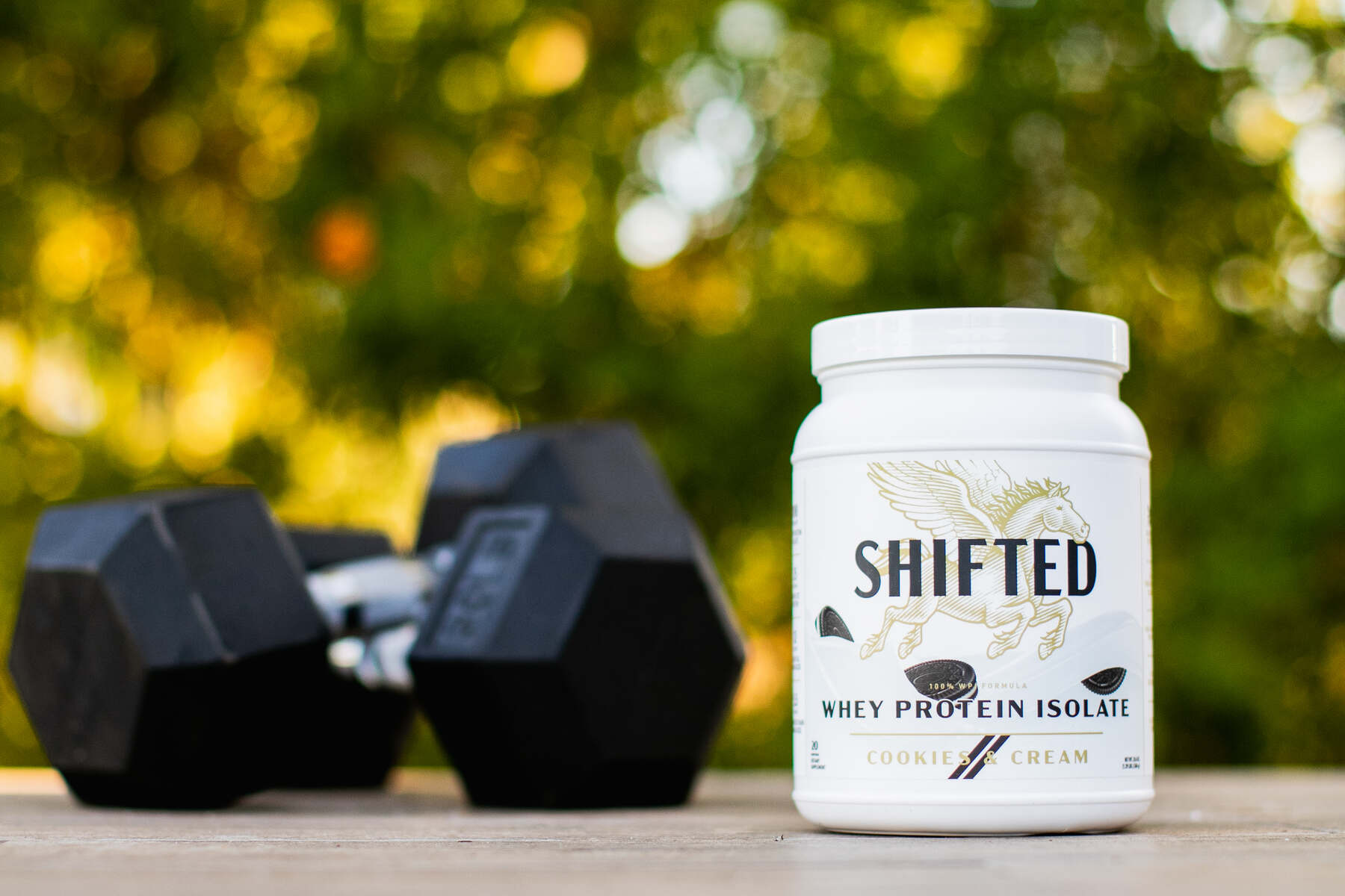 Shifted Whey Protein Isolate in Cookies and Cream flavor with dumbbells on the background